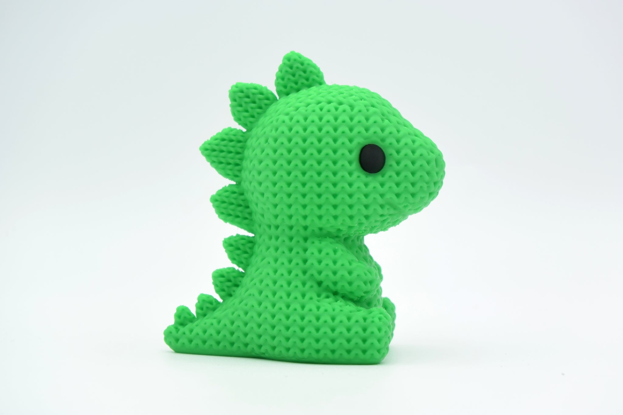 Green knitted stegosaurus dinosaur figurine styled on a wooden shelf beside small plants and books