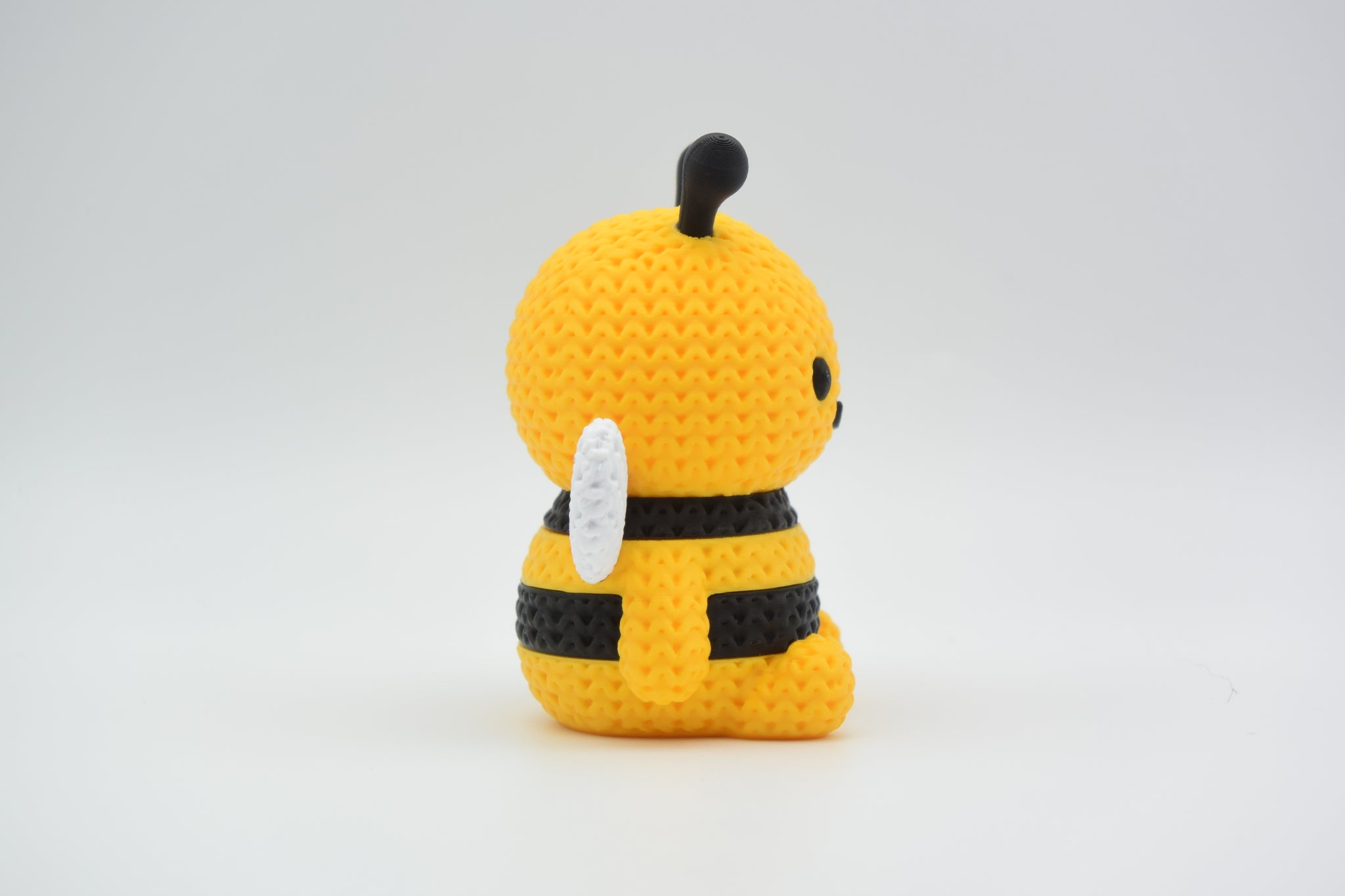 Knitted bee decoration placed on a wooden shelf next to a small potted plant in a bright Scandinavian interior