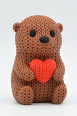 Close-up of a crochet otter figurine holding a small heart, with soft knitted texture detail, on a light surface