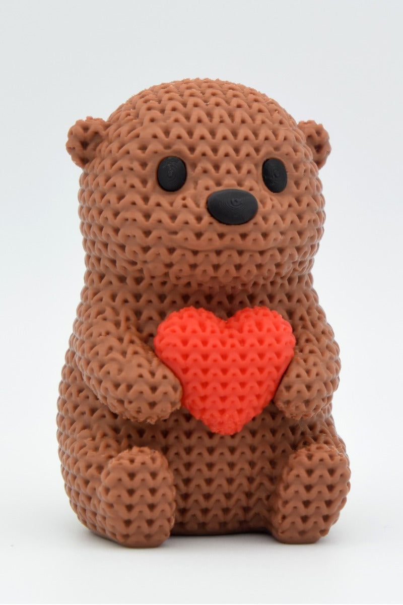 Close-up of a crochet otter figurine holding a small heart, with soft knitted texture detail, on a light surface