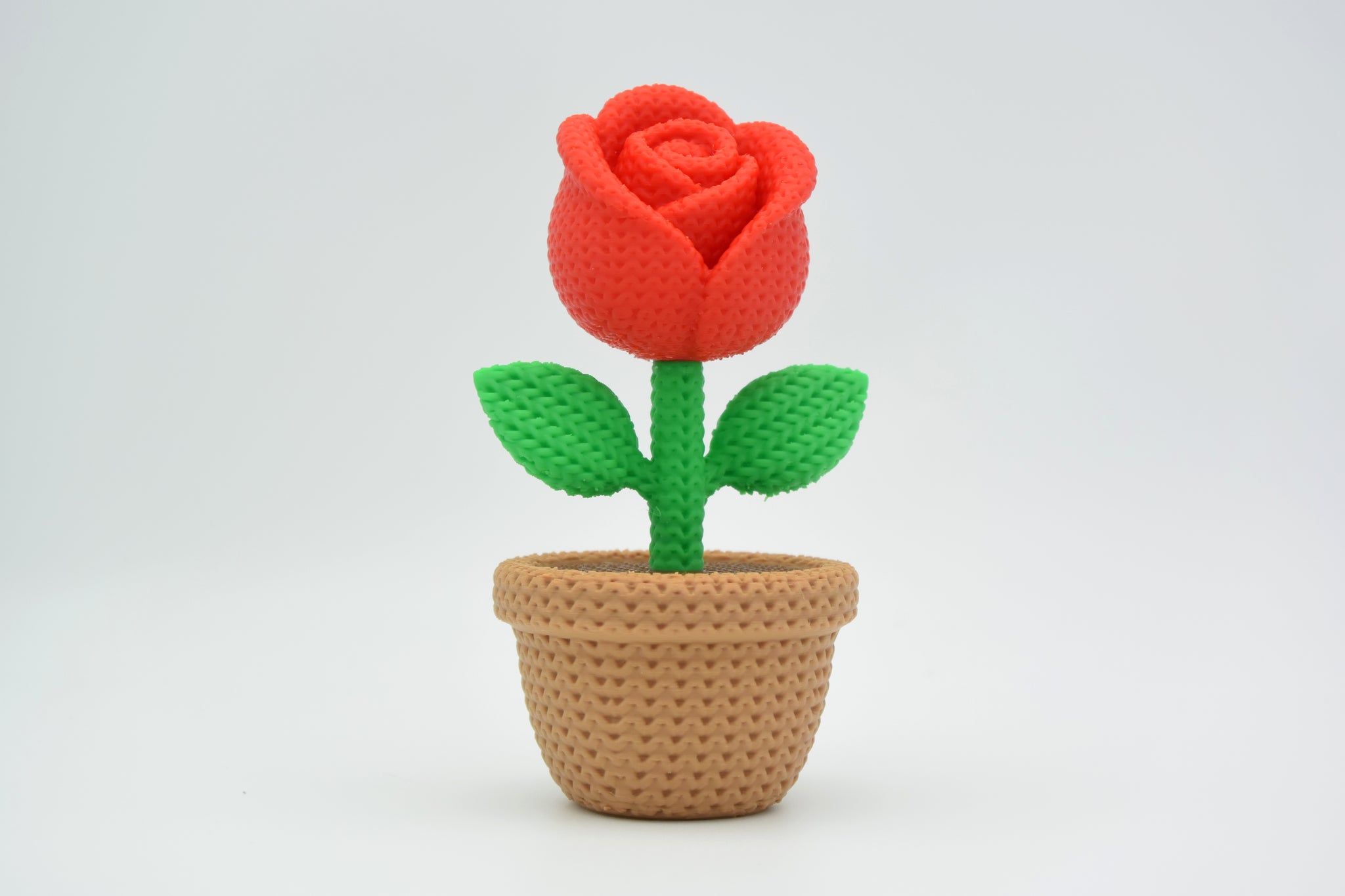 Knitted rose placed on a light wooden shelf next to a candle in a Scandinavian home setting