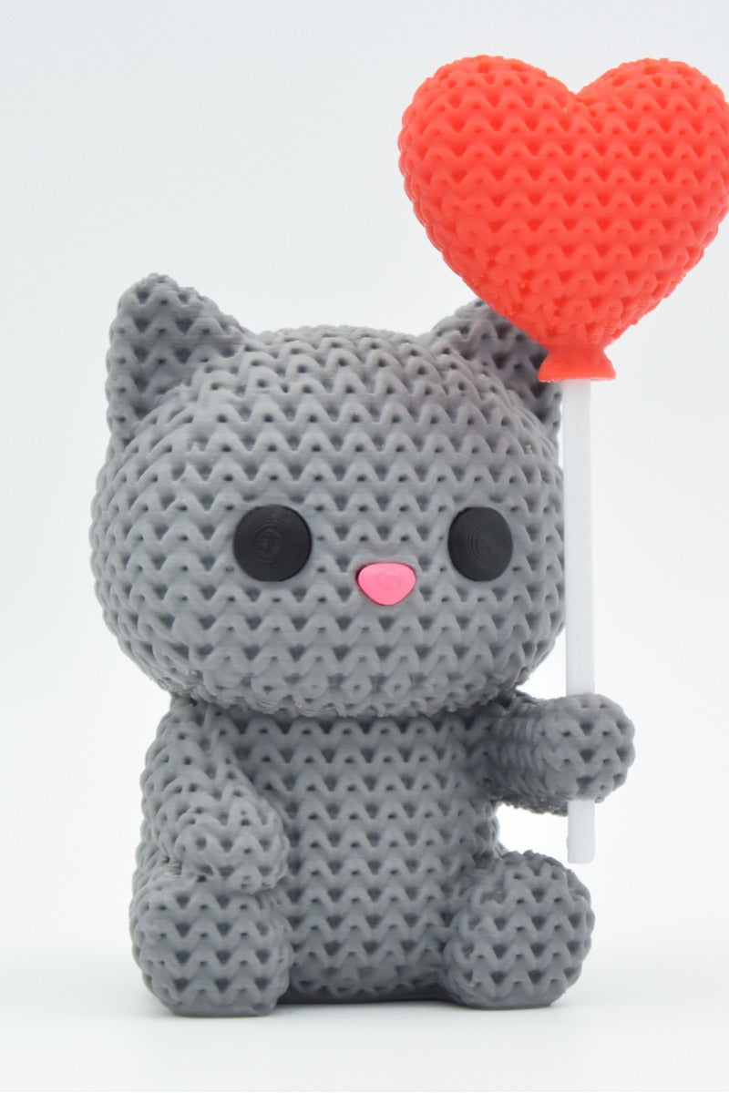 Close-up of a knitted cat figurine holding a heart balloon, showing soft crochet texture in warm tones