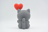 Close-up of a knitted cat figurine holding a heart balloon, showing soft crochet texture in warm tones