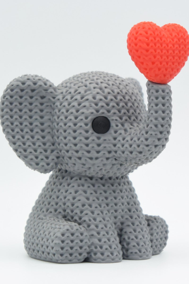 Close-up of a knitted elephant decoration blowing a heart, showing soft crochet-textured surface in warm grey