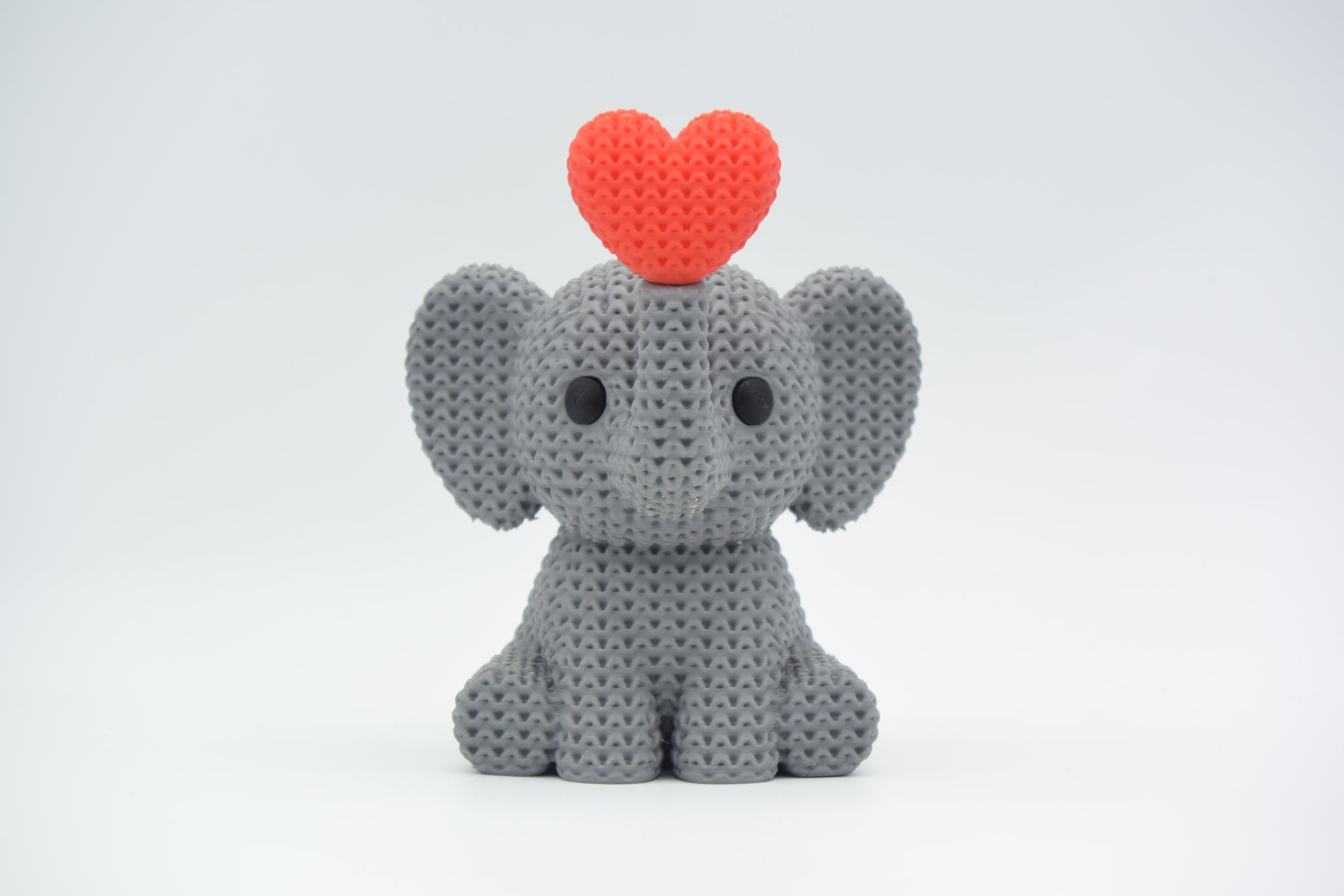 Knitted elephant blowing a heart placed on a wooden shelf beside small Scandinavian home decor items