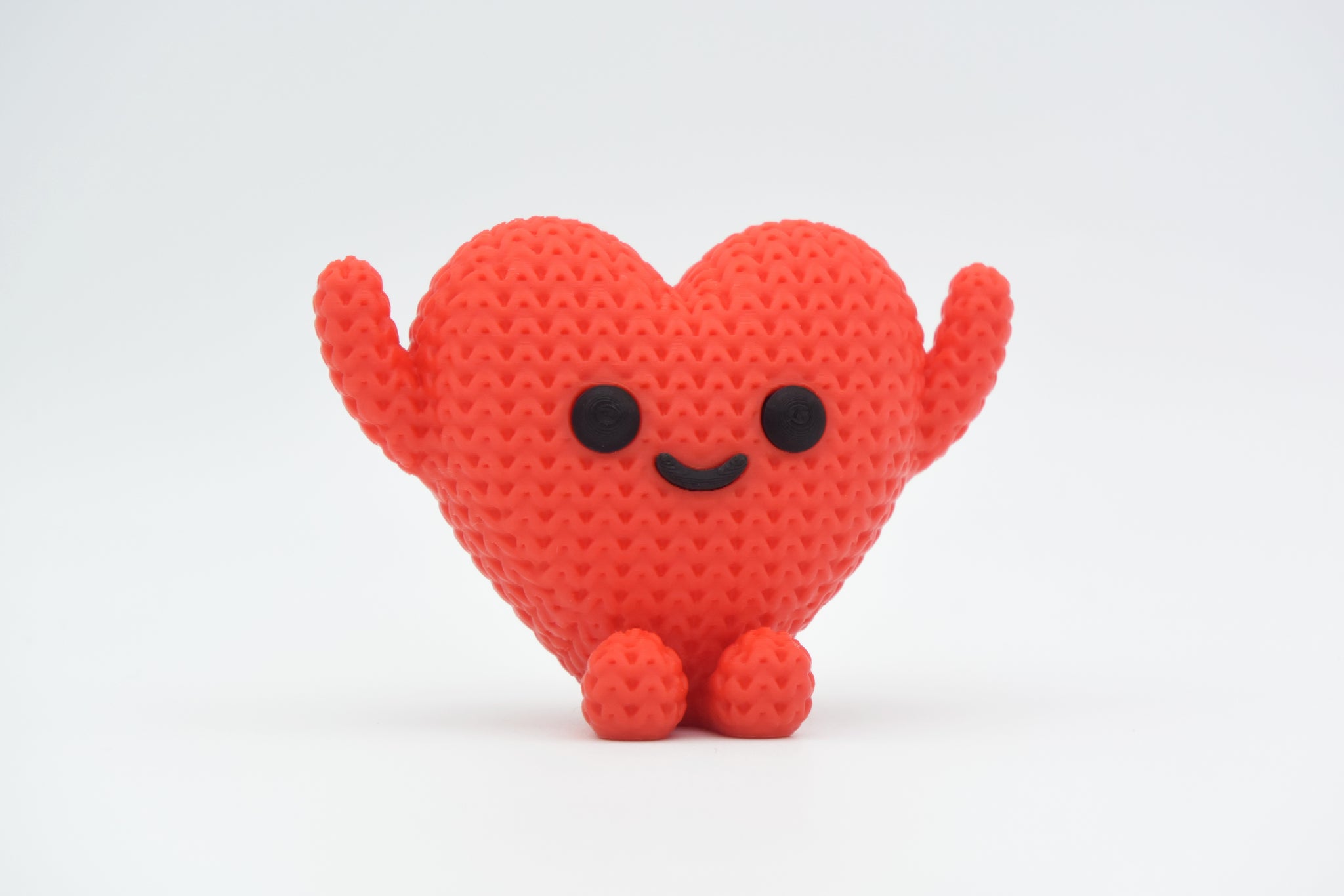Close-up of a small knitted heart figure with a textured crochet surface and a simple character face, in red