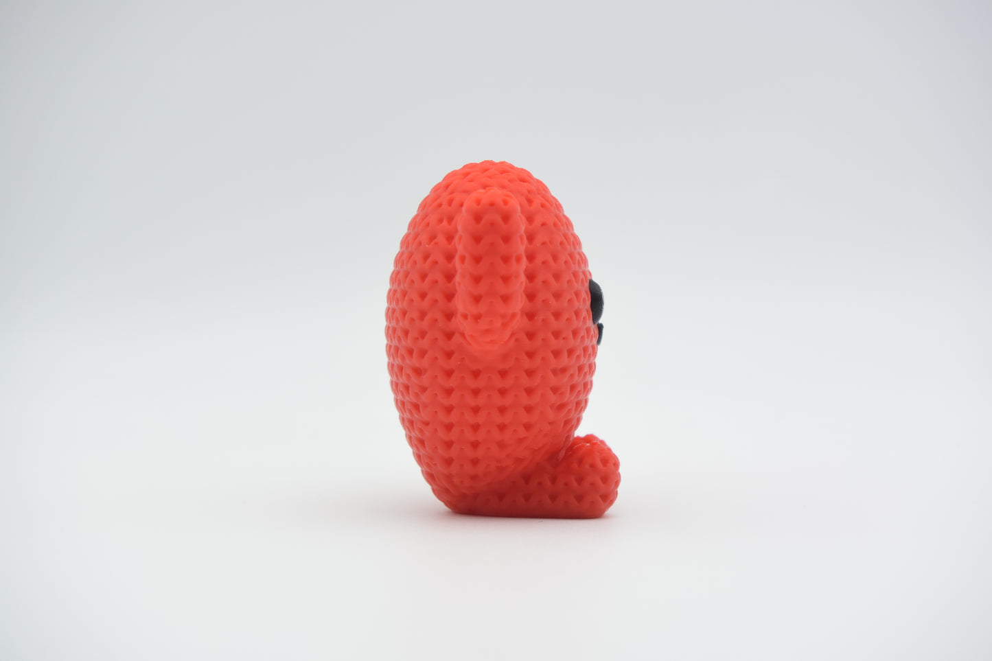 Close-up of a small knitted heart figure with a textured crochet surface and a simple character face, in red