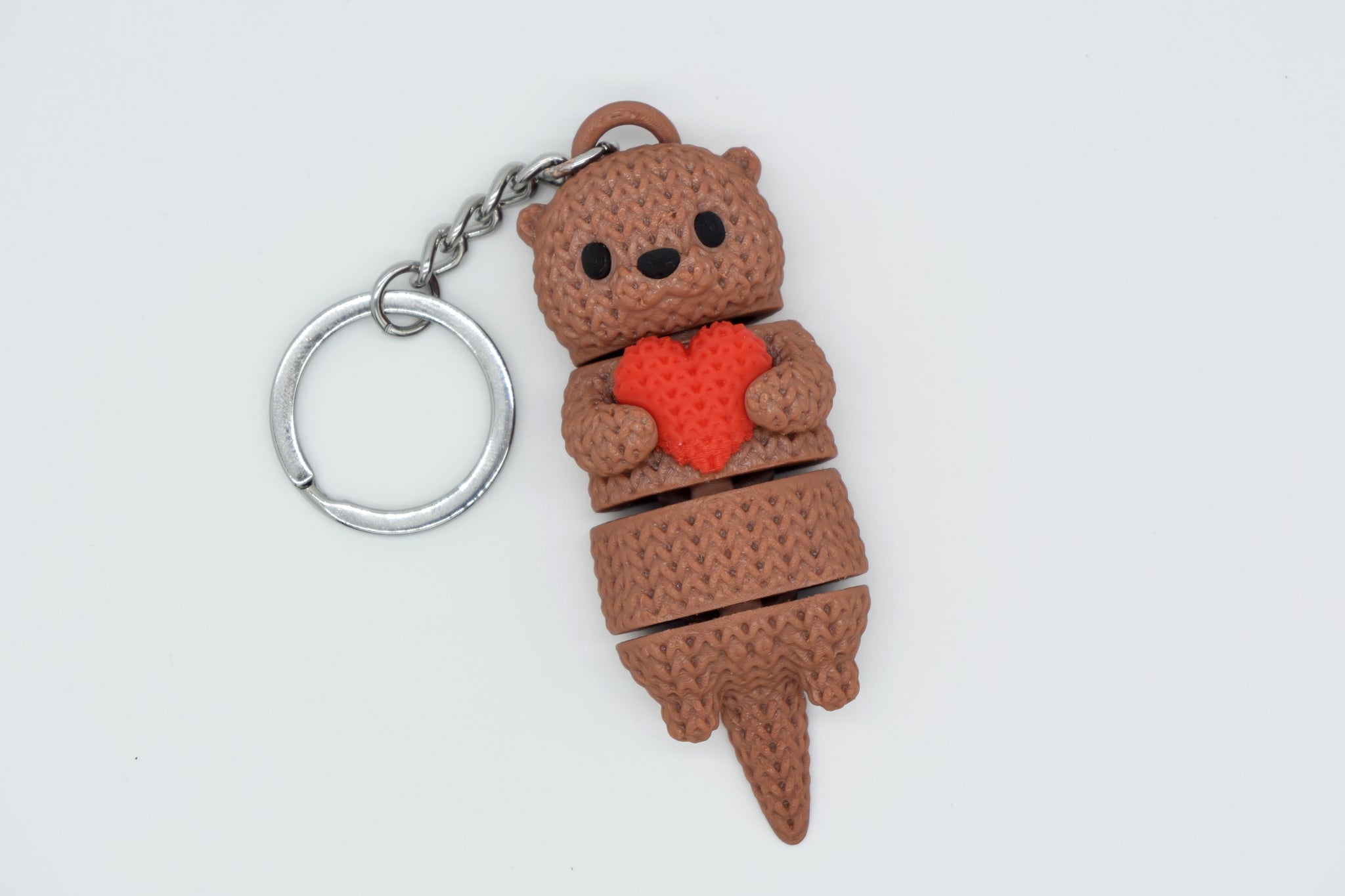 Close-up of a knitted articulated otter holding a small heart, showing soft crochet-texture surface detail