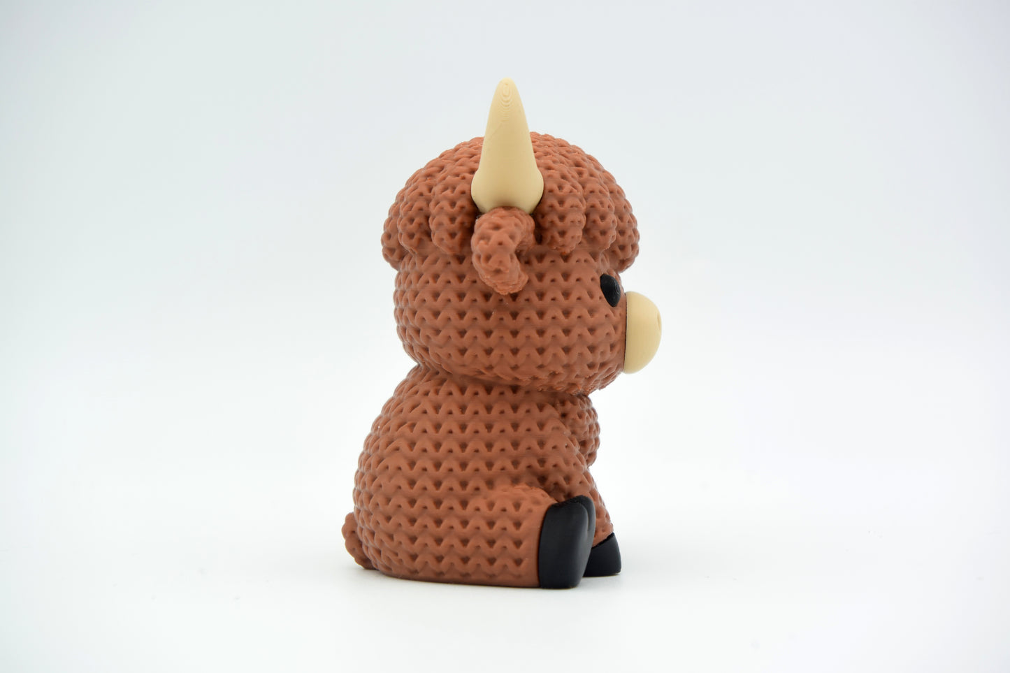 Knitted highland cow figurine displayed on a wooden shelf alongside plants and neutral Scandinavian decor
