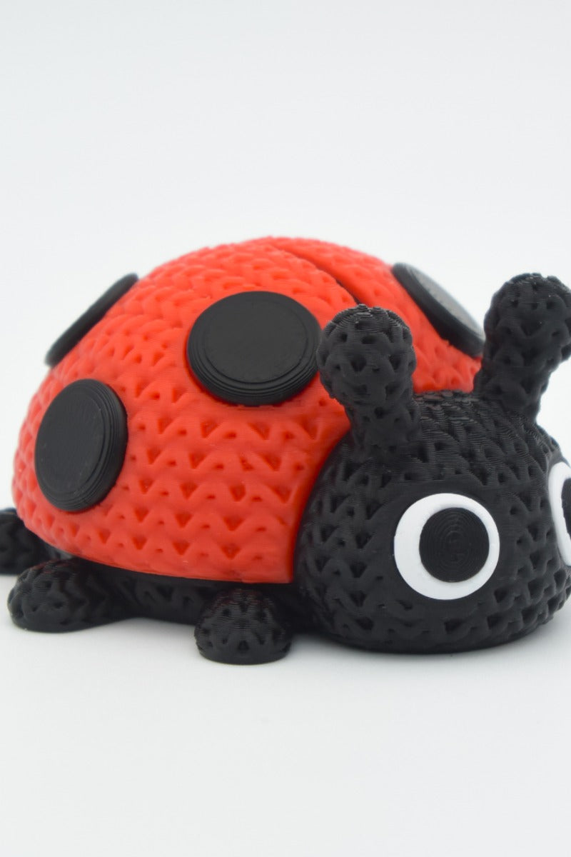 Close-up of a knitted ladybug figure with red and black crochet-look texture on a white surface