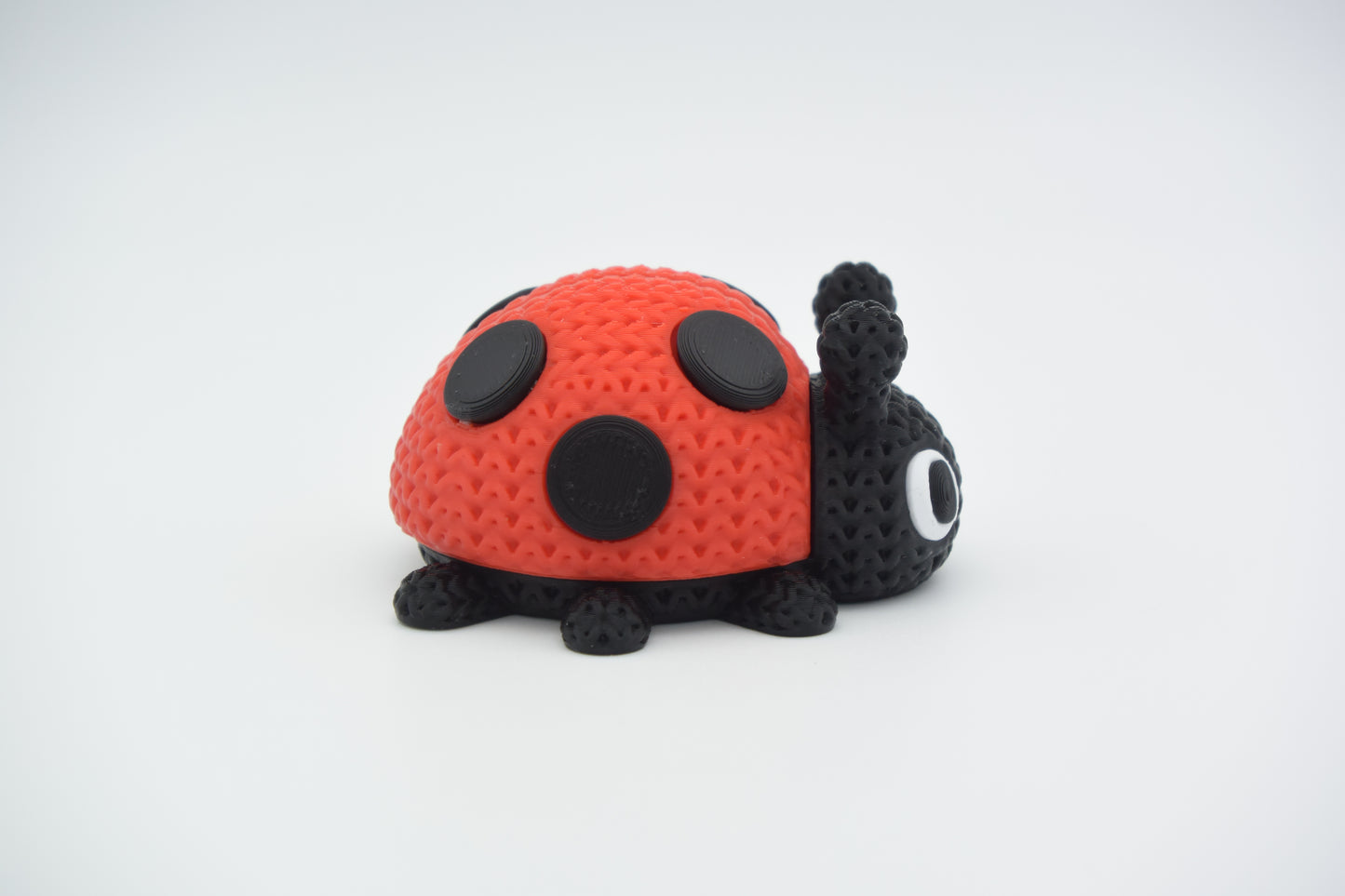 Small decorative knitted ladybug sitting on a wooden shelf beside a plant and neutral home accessories