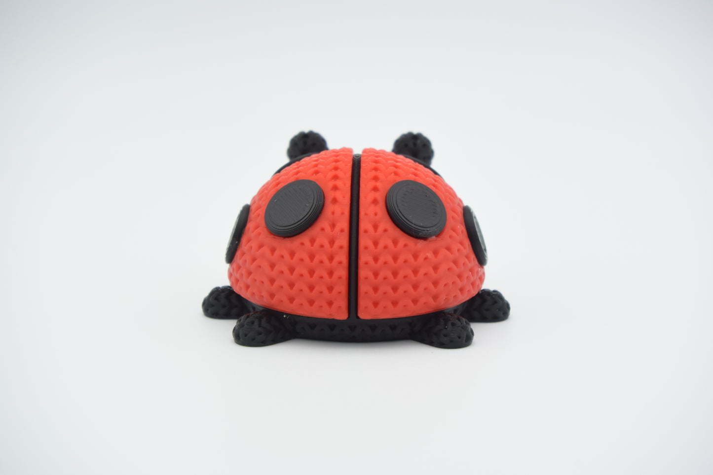 Close-up of a knitted ladybug figure with red and black crochet-look texture on a white surface