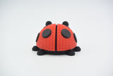 Close-up of a knitted ladybug figure with red and black crochet-look texture on a white surface