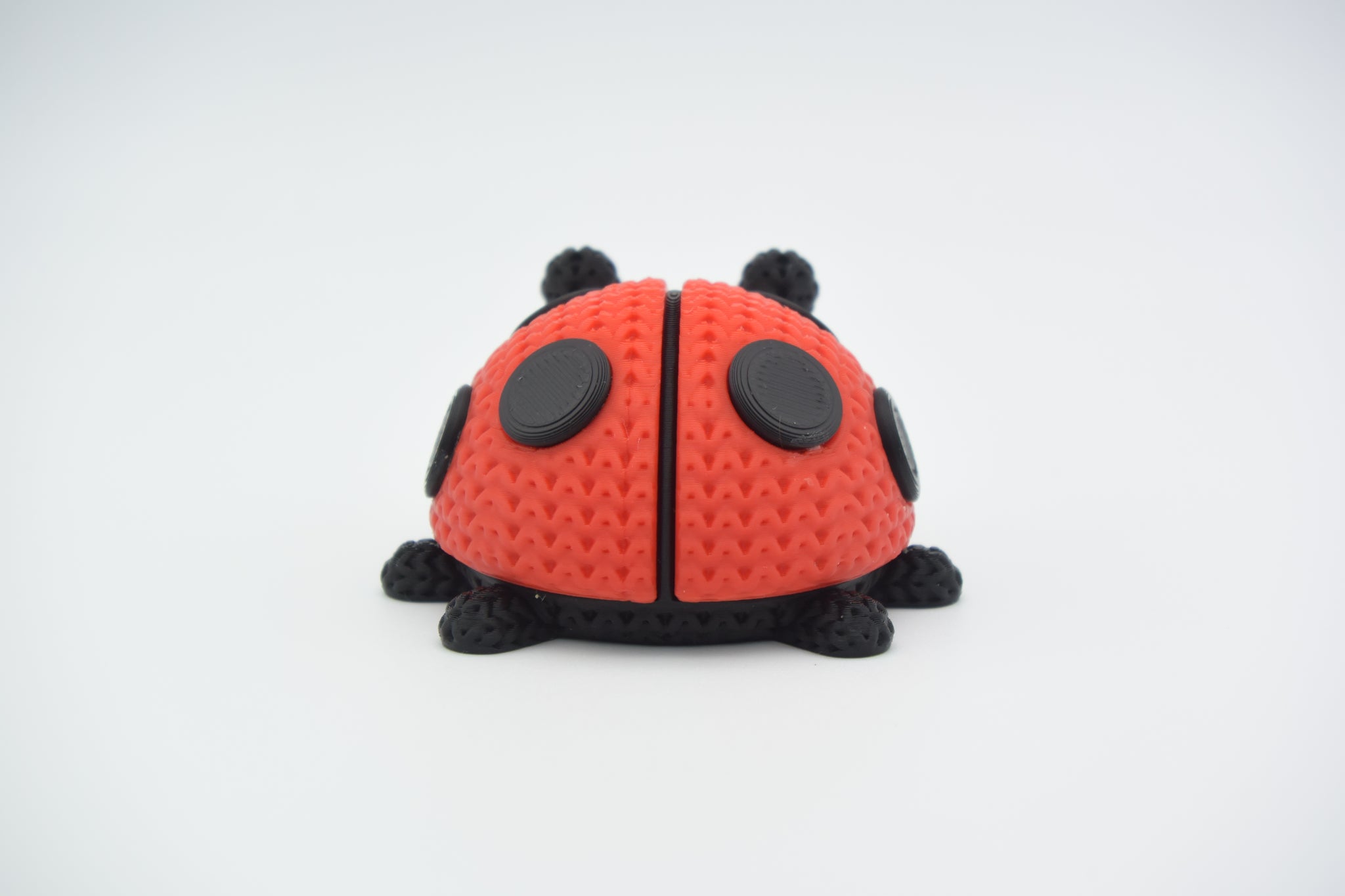 Close-up of a knitted ladybug figure with red and black crochet-look texture on a white surface