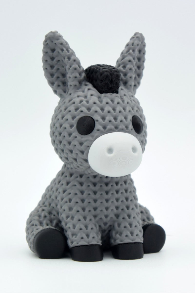 Close-up of a knitted donkey figurine with a soft crochet-look texture, photographed against a neutral background