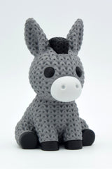 Close-up of a knitted donkey figurine with a soft crochet-look texture, photographed against a neutral background
