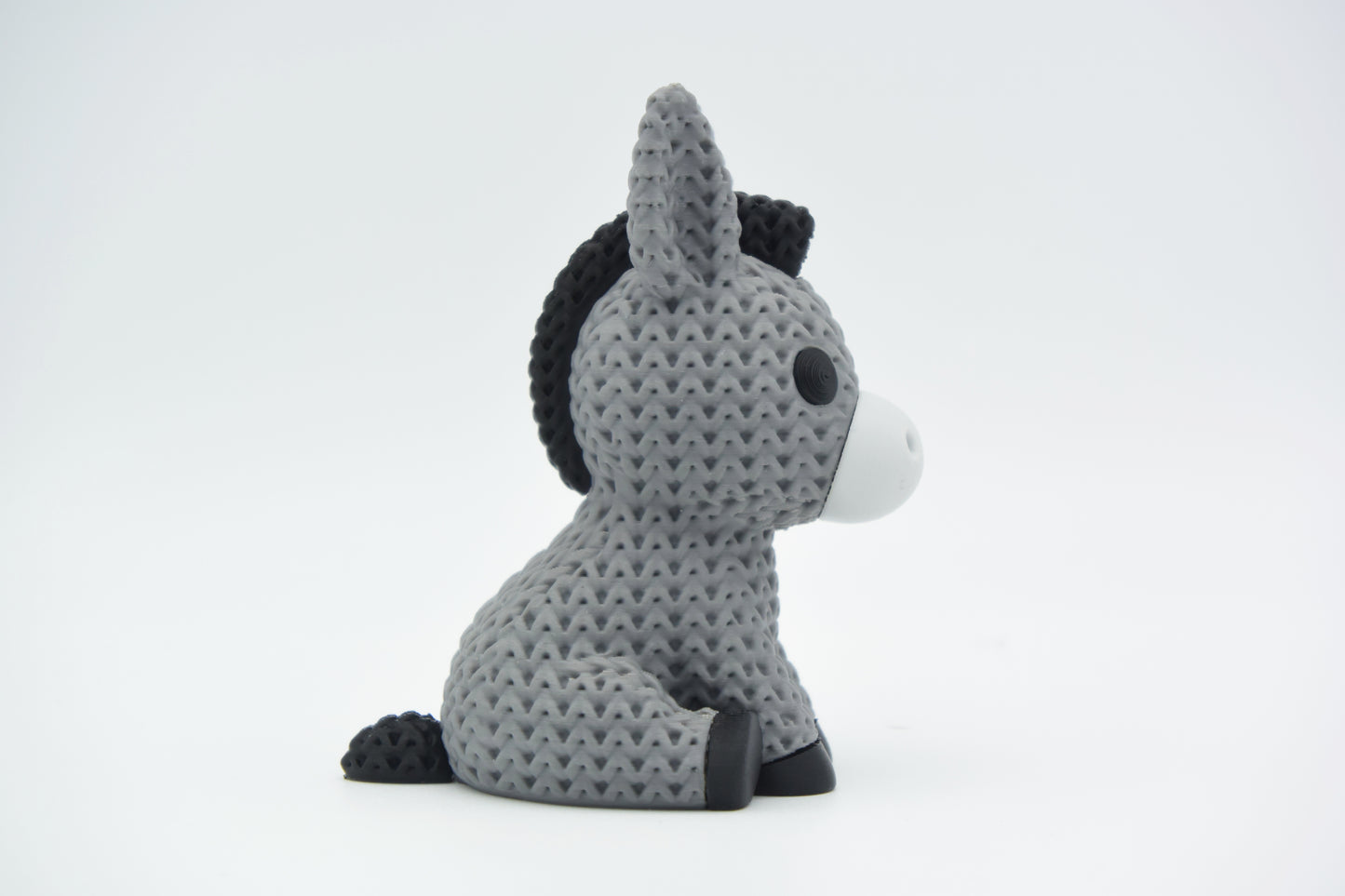 Knitted donkey figurine styled on a wooden shelf next to small plants and Scandinavian home decor