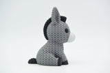Knitted donkey figurine styled on a wooden shelf next to small plants and Scandinavian home decor
