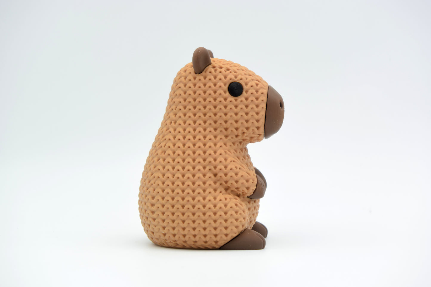 Small knitted capybara decorative figure placed on a wooden shelf beside plants and books in a Scandinavian interior