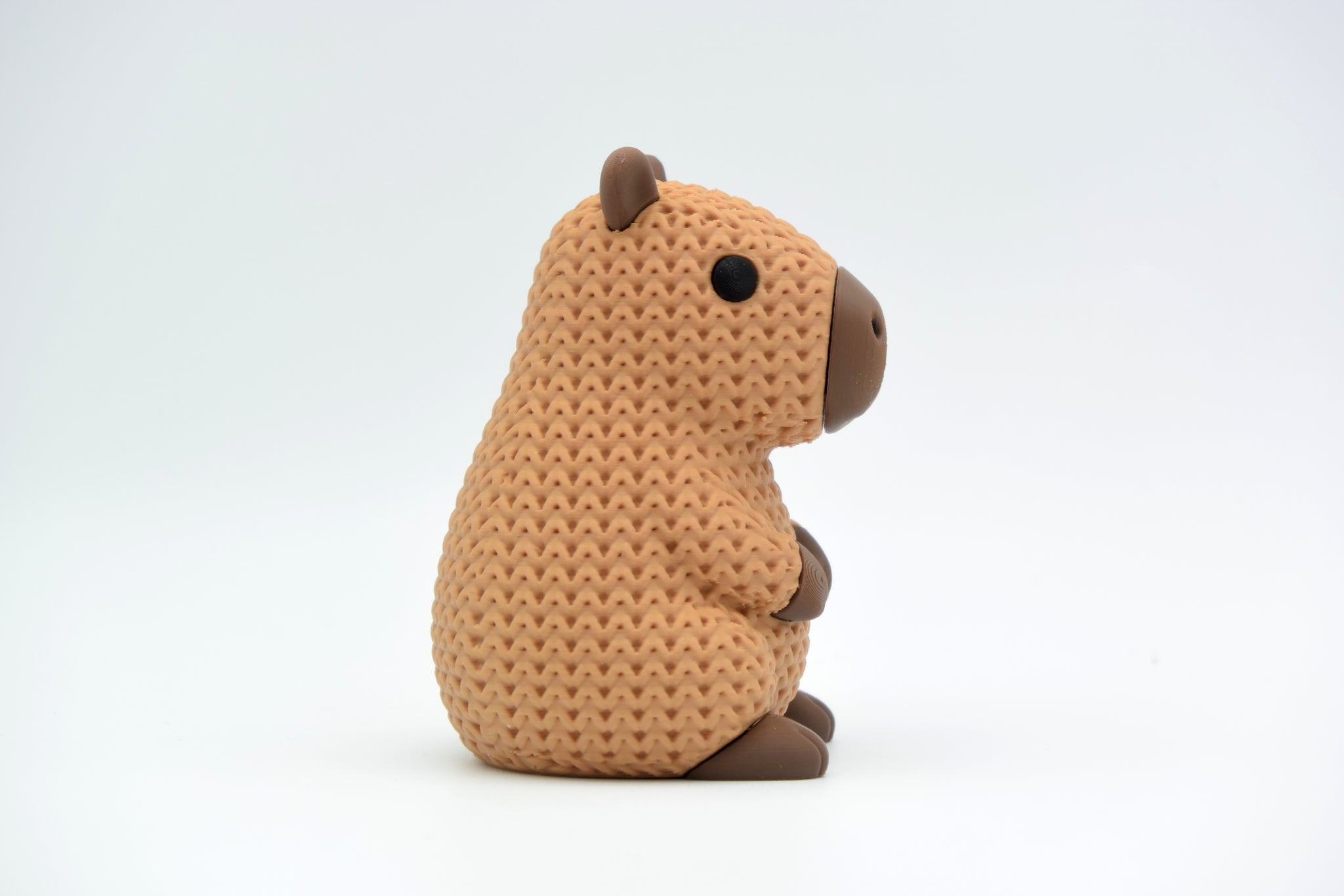 Small knitted capybara decorative figure placed on a wooden shelf beside plants and books in a Scandinavian interior