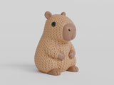 Close-up of a knitted capybara figure with soft crochet texture in warm brown tones, on a white surface