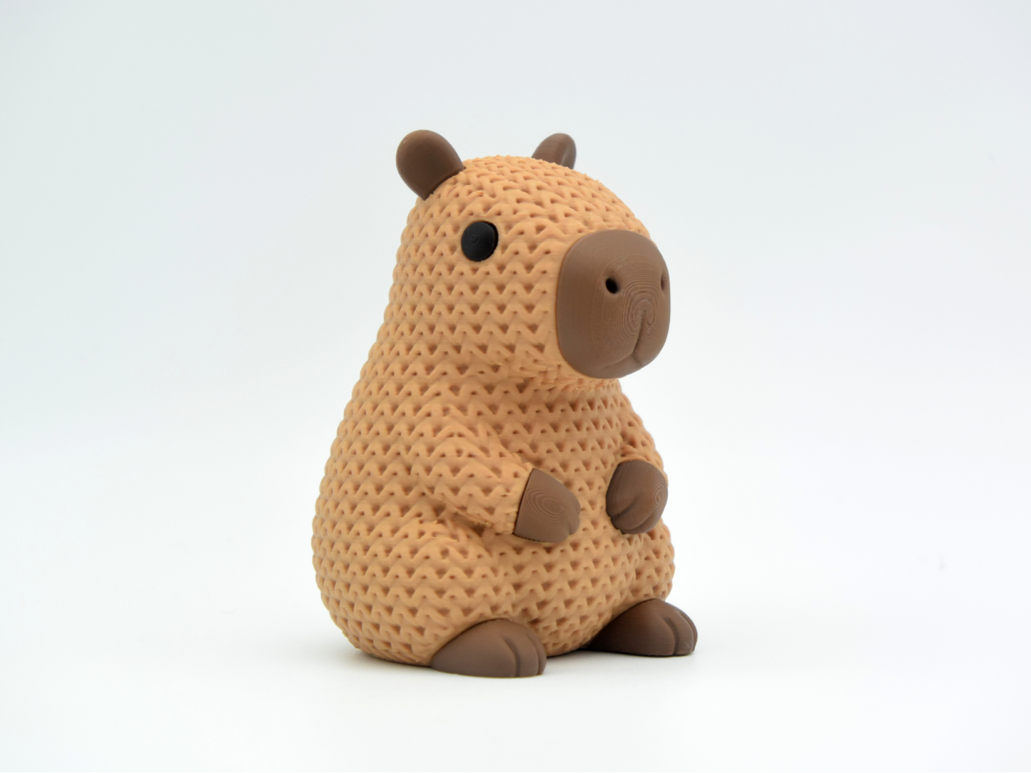 Close-up of a knitted capybara figure with soft crochet texture in warm brown tones, on a white surface