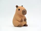 Close-up of a knitted capybara figure with soft crochet texture in warm brown tones, on a white surface