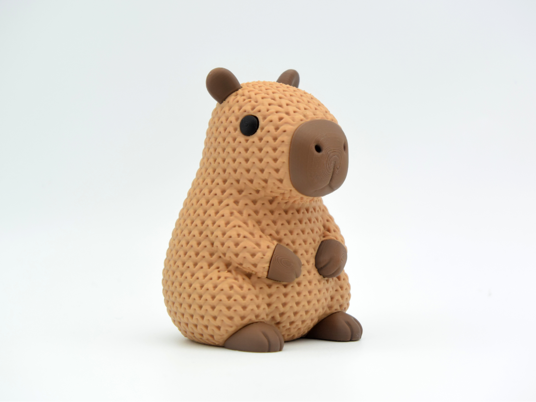 Close-up of a knitted capybara figure with soft crochet texture in warm brown tones, on a white surface
