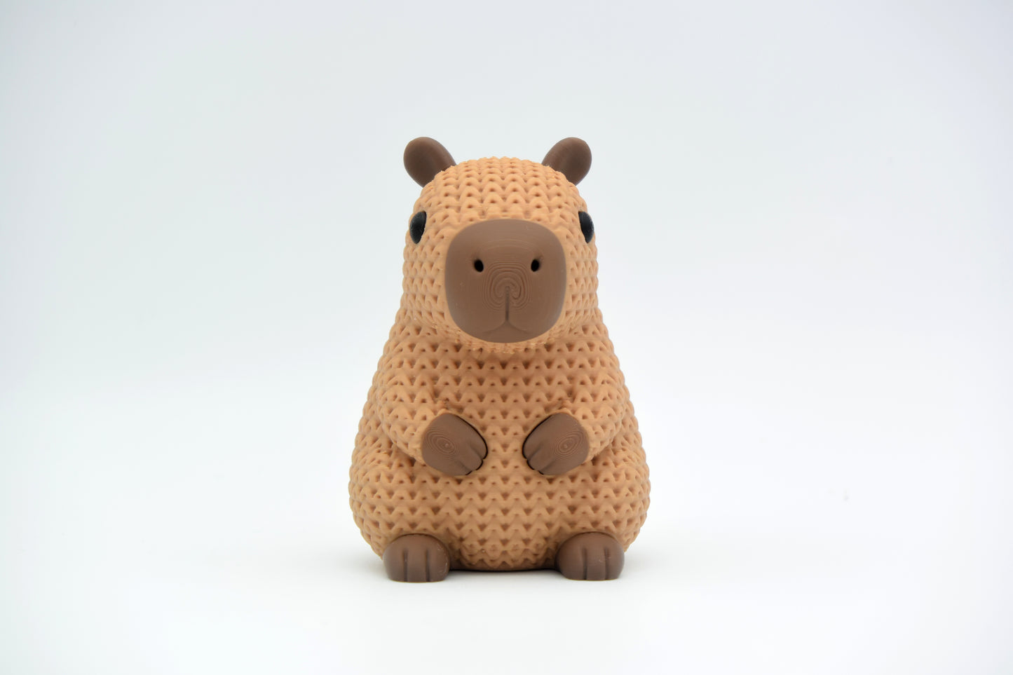Close-up of a knitted capybara figure with soft crochet texture in warm brown tones, on a white surface