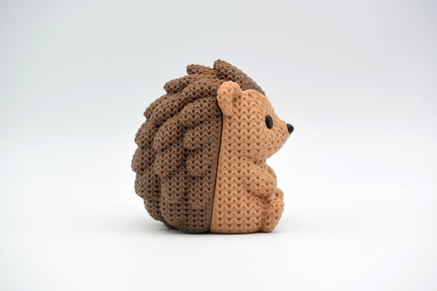 Small knitted hedgehog decoration placed on a wooden shelf beside a candle and a few dried leaves