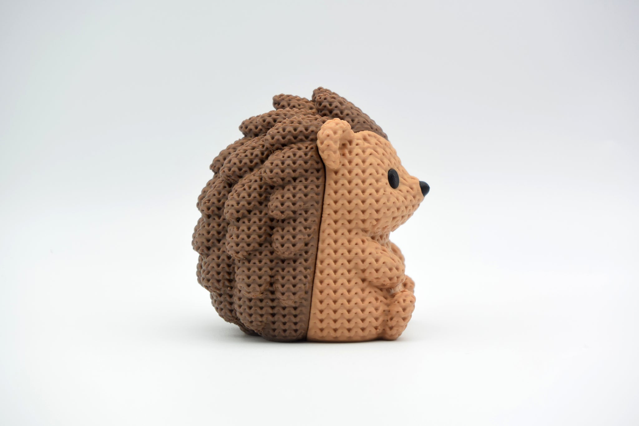 Small knitted hedgehog decoration placed on a wooden shelf beside a candle and a few dried leaves