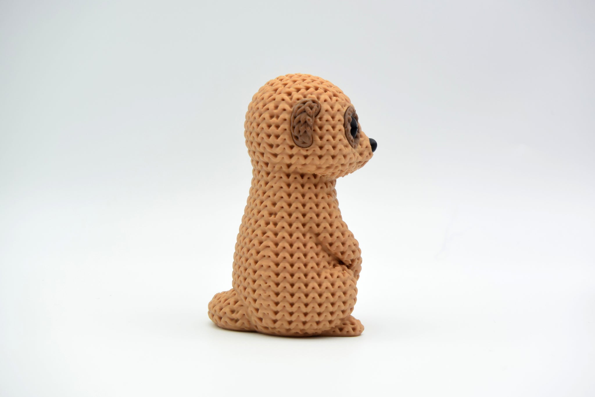 Knitted meerkat figurine styled on a wooden shelf beside a small plant and neutral home decor objects