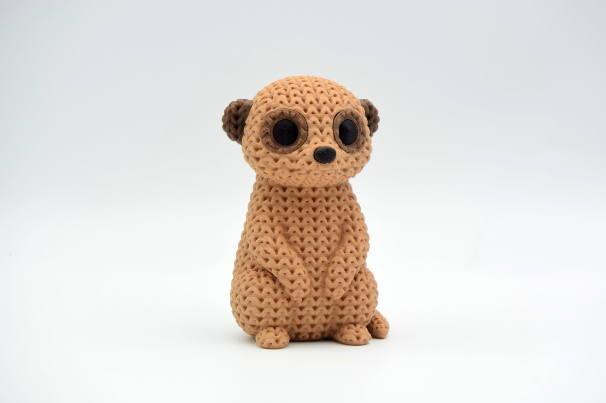 Close-up of a knitted meerkat figurine with a crochet-texture surface, standing upright on a white background