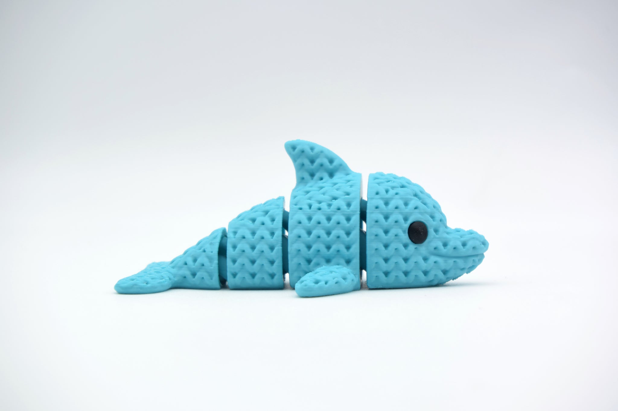 Small knitted dolphin figurine resting on a wooden shelf beside books and a plant in a Scandinavian home interior