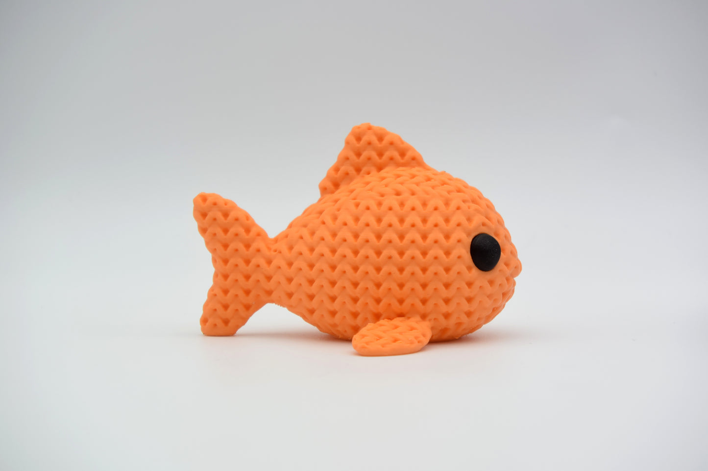 Knitted fish decoration placed on a wooden shelf beside a small plant and ceramic bowl