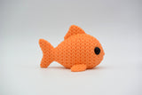 Knitted fish decoration placed on a wooden shelf beside a small plant and ceramic bowl