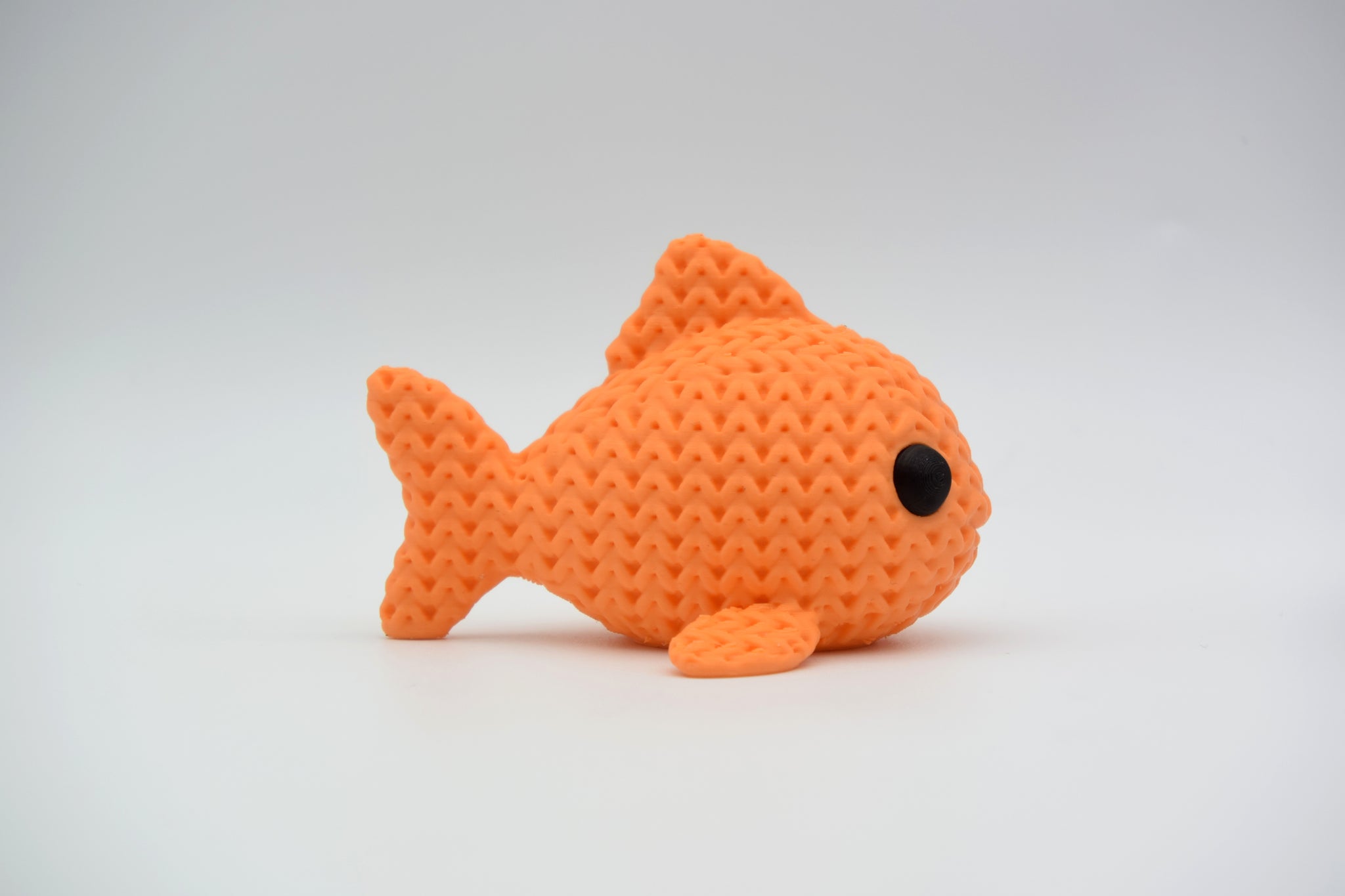 Knitted fish decoration placed on a wooden shelf beside a small plant and ceramic bowl
