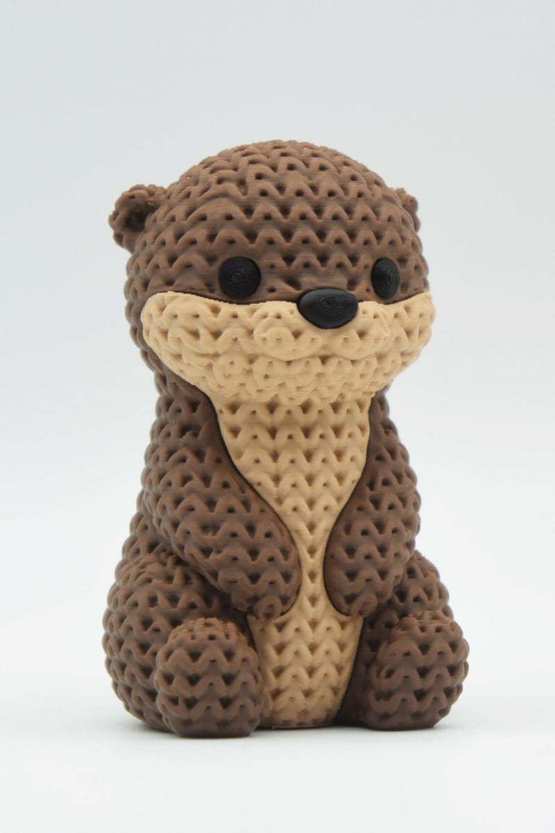 Close-up of a knitted otter figurine with a soft crochet-texture surface and detailed face, shown on a white background