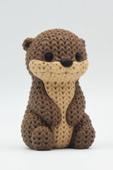 Close-up of a knitted otter figurine with a soft crochet-texture surface and detailed face, shown on a white background