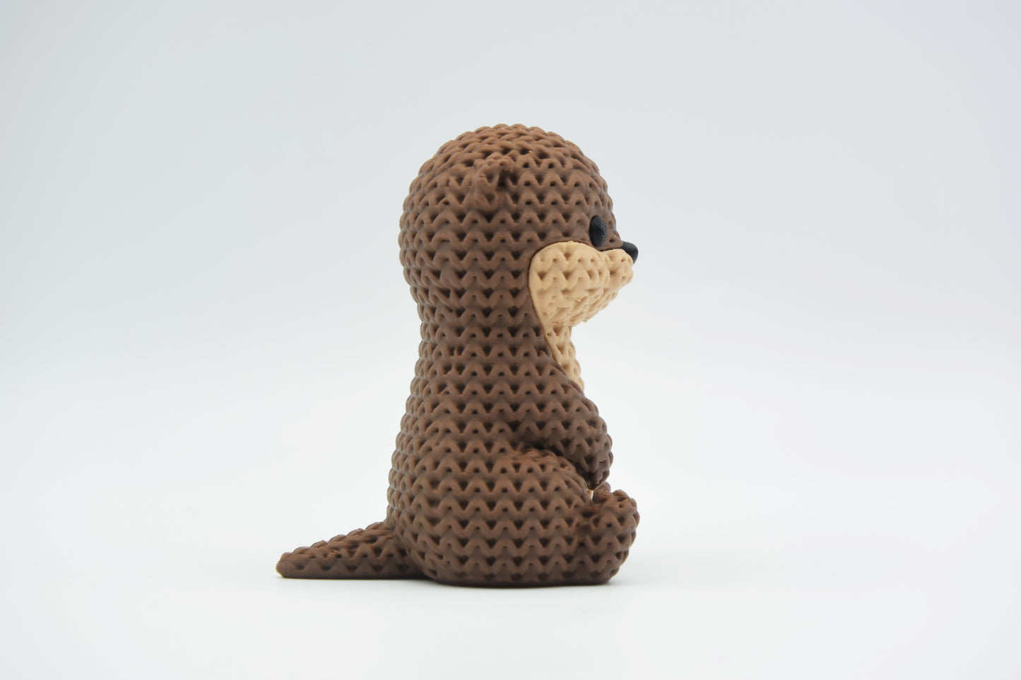 Close-up of a knitted otter figurine with a soft crochet-texture surface and detailed face, shown on a white background