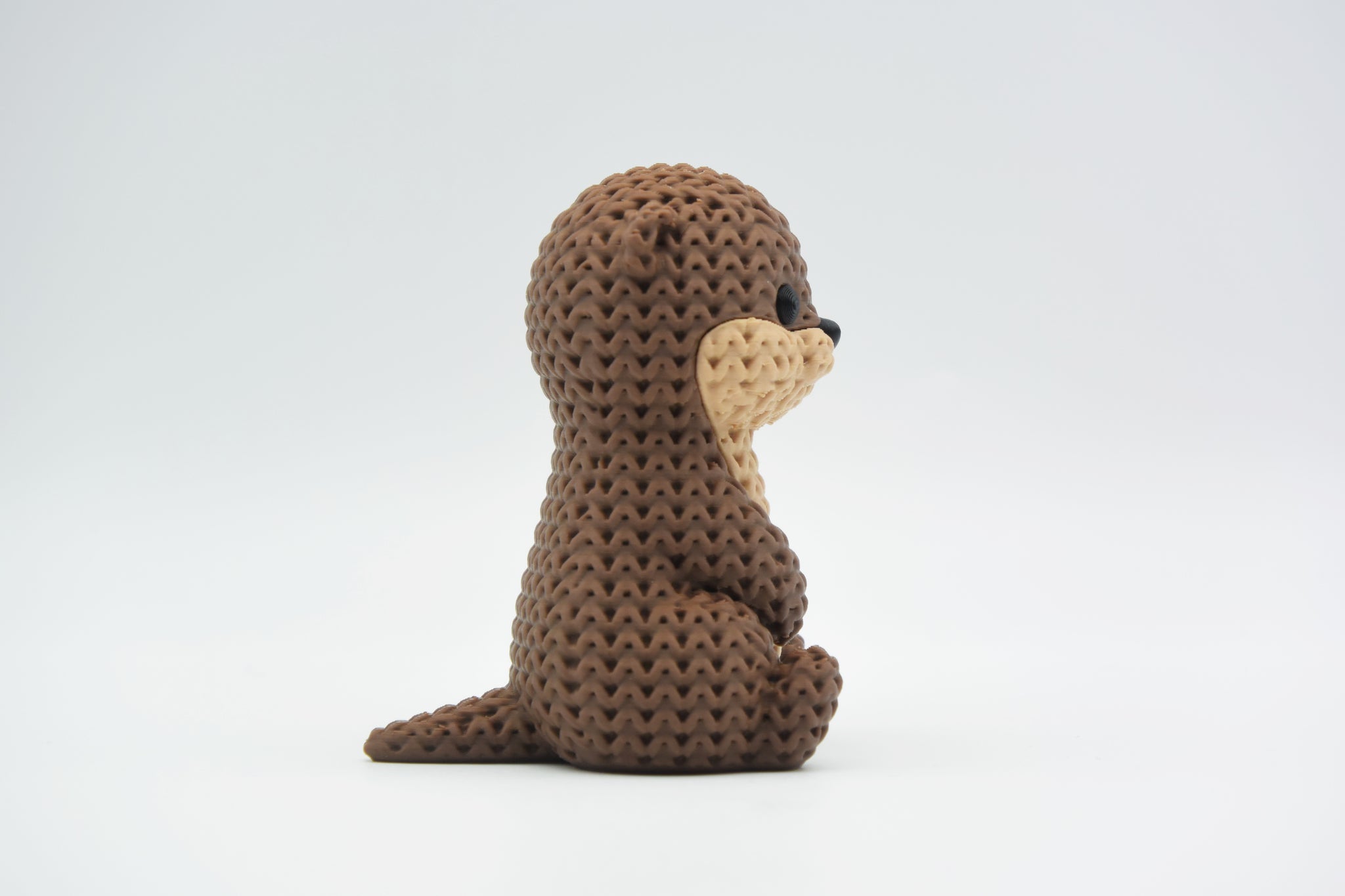 Close-up of a knitted otter figurine with a soft crochet-texture surface and detailed face, shown on a white background