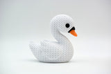 White knitted swan decoration styled on a wooden shelf beside dried flowers and neutral home decor
