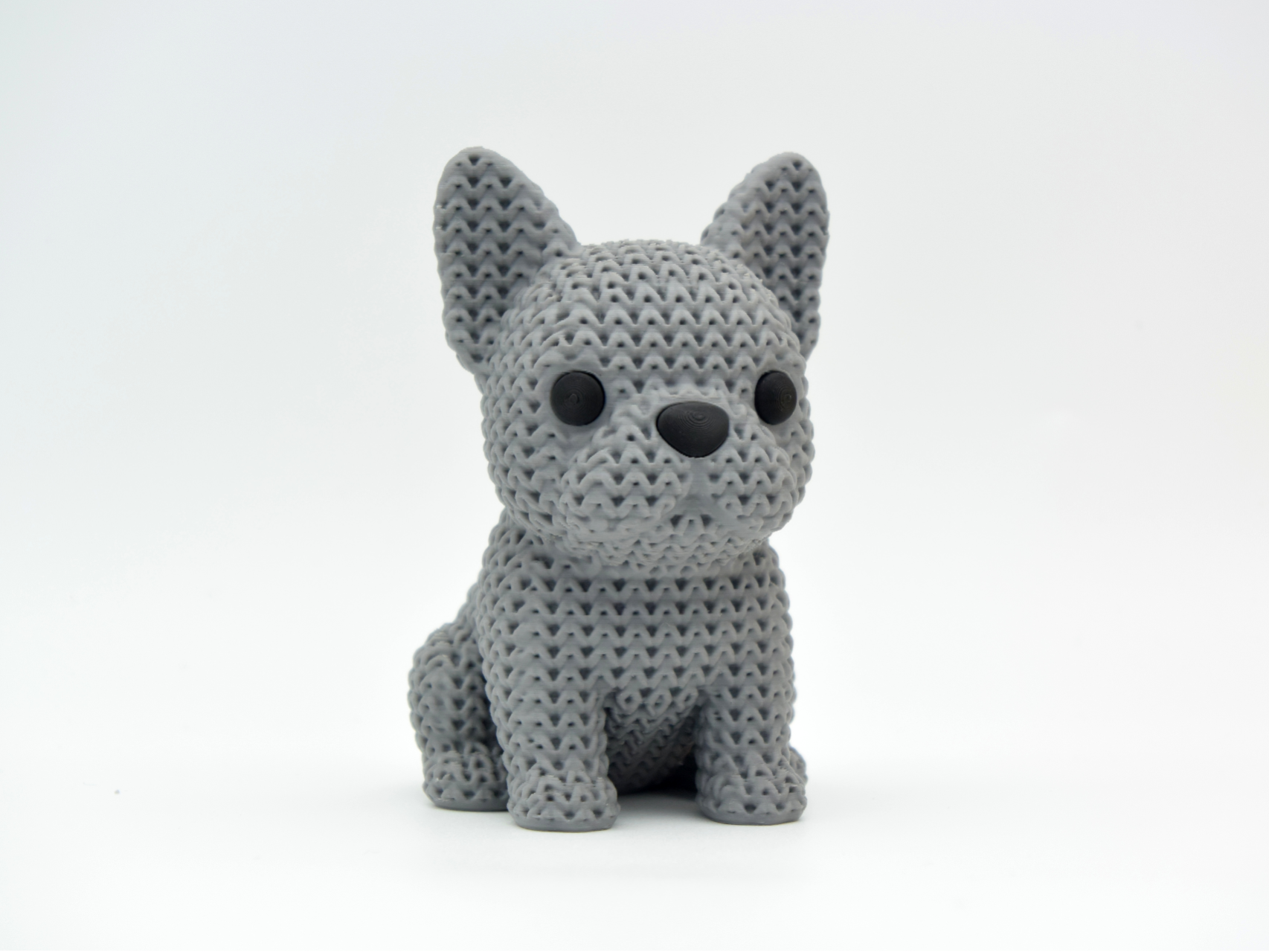 Close-up of a knitted French Bulldog decorative figure with a textured crochet-like coat, shown on a light surface