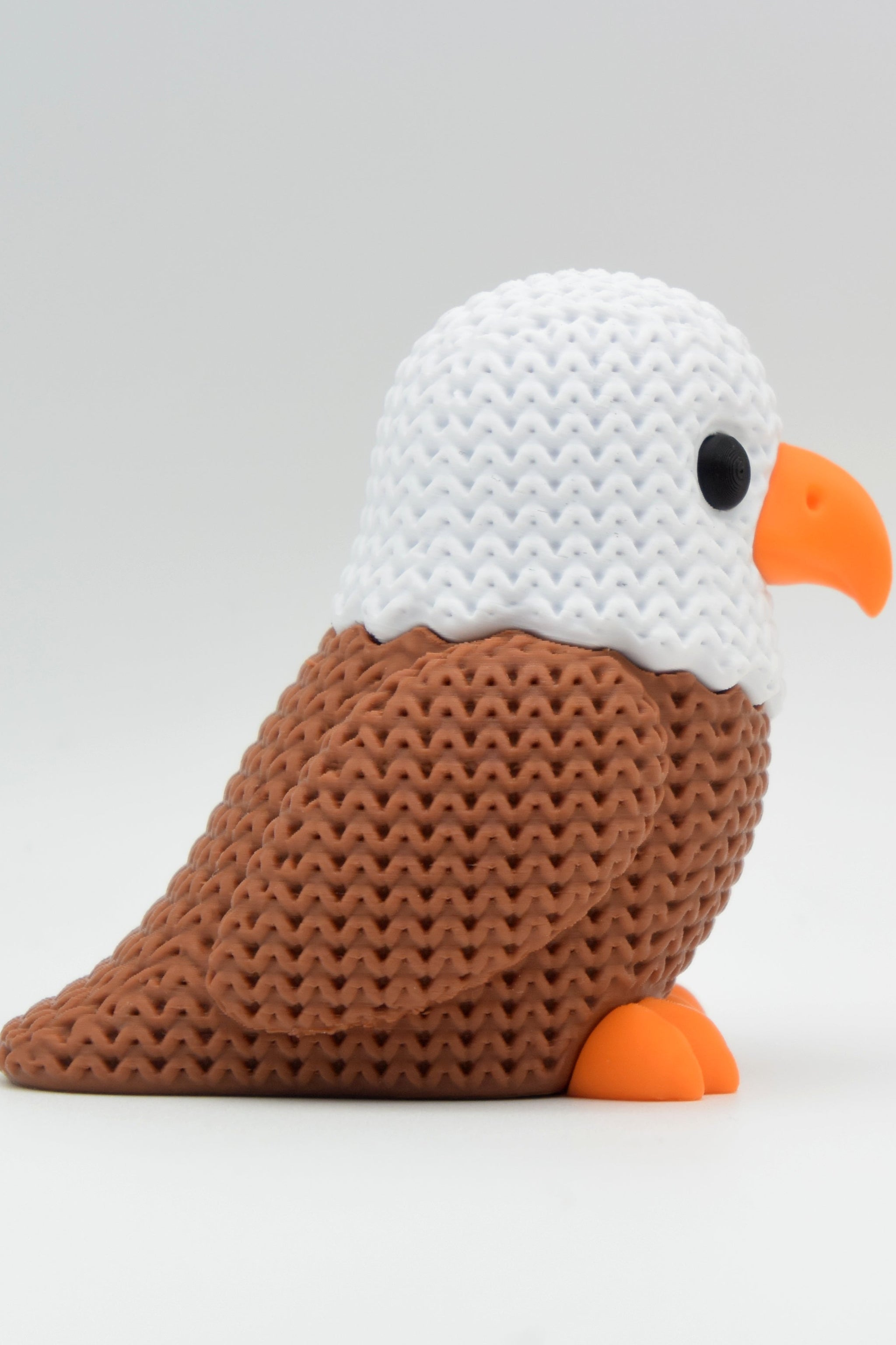 Close-up of a knitted eagle figurine with crochet-look texture and detailed feather ridges, shot on a white surface