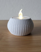 Close-up of a knitted tea light holder with a soft woven texture, unlit, on a white surface
