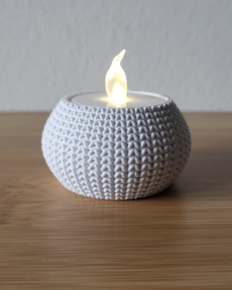 Close-up of a knitted tea light holder with a soft woven texture, unlit, on a white surface