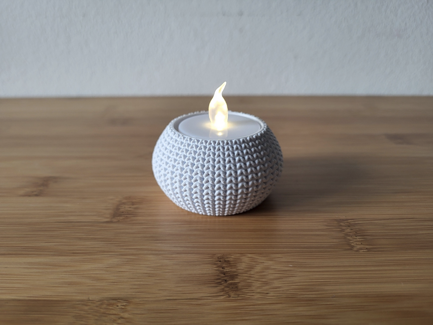 Knitted tea light holder with a glowing tea light on a wooden shelf in a cosy home interior