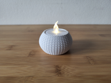 Knitted tea light holder with a glowing tea light on a wooden shelf in a cosy home interior
