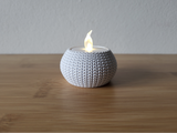 Close-up of a knitted tea light holder with a soft woven texture, unlit, on a white surface