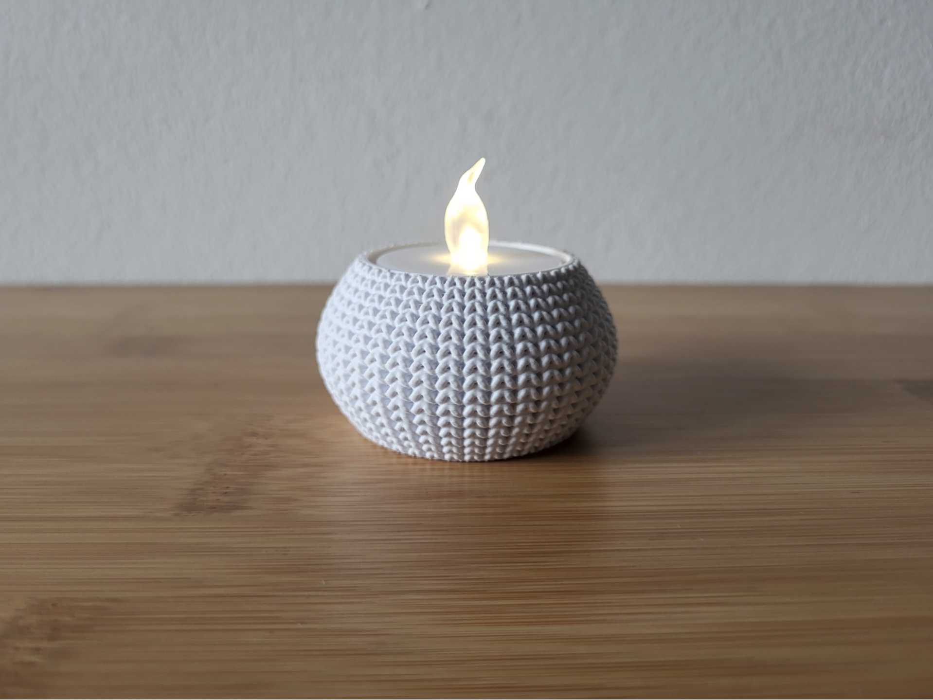 Close-up of a knitted tea light holder with a soft woven texture, unlit, on a white surface